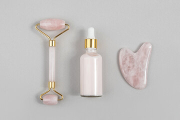 Crystal rose quartz facial roller, massage tool Gua sha and anti-aging collagen, serum in glass bottle on grey background. Facial massage for natural lifting, Beauty concept Top view