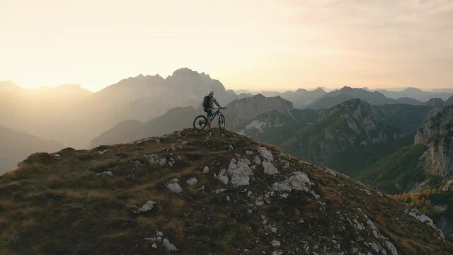 Aerial - Extreme mountain male biker resting at the cliff of the mountain enjoying the view on a beautiful summer day. 4K
