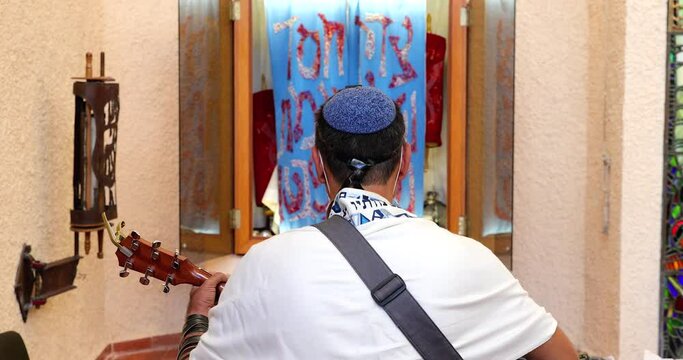 Rabbi of the Jewish Reform movement is wrapped in a Tallit, prays, and plays the guitar in front of the Torah ARK.