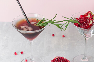 Cold non-alcoholic pomegranate cocktail with rosemary on a light pink background. Fruit grains in a glass. Natural healthy drink