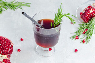 Pomegranate non-alcoholic cocktail with rosemary on a light background. Fruit grains in a glass....