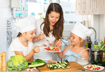Portrait of happy family of mother and two daughters eating freshly cooked salad at home kitchen