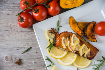 Grilled salmon steak on vintage wooden board with fork, olive oil, vegetables, herbs and spices on dark concrete background. Raw salmon fillet with vegetables, spices and lemon on wooden table.