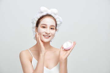 Happy young Asian woman applying facial clay mask and wearing a towel.