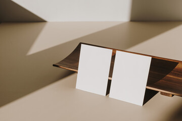 Blank paper sheet cards with mockup copy space and wooden tray with sunlight shadow on beige table. Minimal business brand template