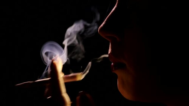 Beautiful profile silhouette of attractive woman on black background smoking cigarette inhaling exhaling dense smoke