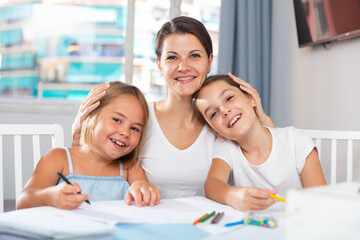 Happy girls with mom draw at the table at home