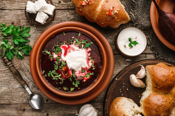 Obraz na płótnie Canvas Ukrainian and Russian traditional beet root soup or borscht in bowl with rib eye meat, sour cream, buns, goat cheese, garlic, parsley on a wooden rustic background. Healthy food, top view