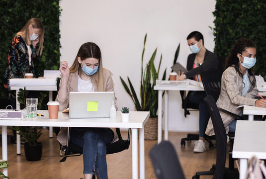 Group of a young female freelancers with mask working in an office while sitting at a table with colleagues.
