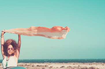 Concept of freedom and beautiful travel middle age adult woman - people enjoy free space and wind - woman with orange pareo and blue coloured sky in background