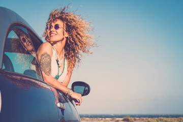 Attractive curly blonde young woman smile and enjoy the wind outside the car - concept of beauty and travel for happy and cheerful caucasian people - alternative lifestyle female feel the freedom joy - Powered by Adobe