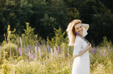 Young blonde with short hair in a summer white dress. Woman poses in a lupine field