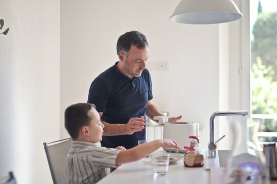 European Father And Son Making Breakfast In The Kitchen