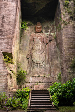 Giant relief image of Japanese hyaku-shaku kannon buddha carved in excavated stone wall cavity covered with moss and climbing plant leaves in Mount Nokogiri stone quarry.