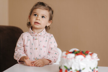 Cute little girl one and a hulf year old stand by delicious birthday cake. Eighteen month old girl verry happy and laughs. Vegetarian food. Lactose free and gluten free.