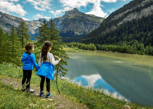 Two girls stands by a lake during a hike in the Swiss alps in Valais, Conthey, Derborence. Lake Derborence was formed in 1749 after two landslides coming from the south wall of the Diablerets.