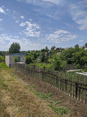 Fototapeta na wymiar Kamen-na-Obi, Altai, Russia - May 22, 2020: Village buildings (cottage) behind a wooden fence. Strawberries, onions, dill and other plants grow on the field. Vertical.