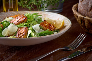 Fresh salad with avocado, arugula and fish fillet, on wooden background close-up. Healthy food.