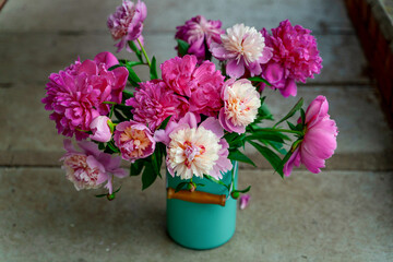 Bouquet of peony flowers in milk can on cement stairs