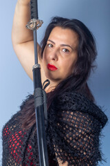 Portrait of a European woman with a sword in her hands. Shooting in the studio. Close-up, red lipstick, model in a black cape.