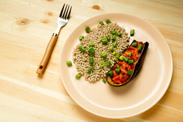 Green buckwheat with baked eggplant with tomato and garlic on a plate with a fork.