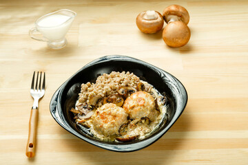 Chicken meatballs with mushrooms in a creamy sauce with a side dish of green buckwheat next to mushrooms and cream.