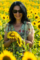 Joyful woman with sunglasses posing with sunflowers
