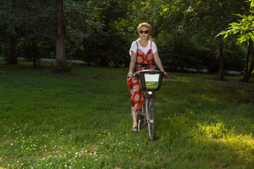 Mature woman rides a bicycle in the evening park. Secluded walk