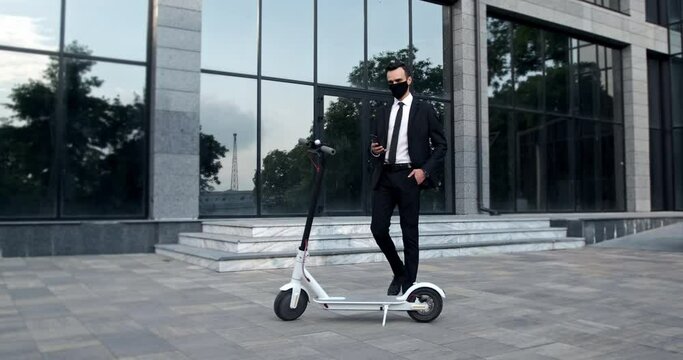 A businessman in a black mask, talking on the phone, goes to his electric scooter and then does authentication with the phone.