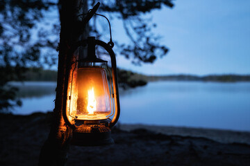 Vintage old kerosene lamp hanging on a tree. Beautiful view of glowing lantern and dark misty lake at night. Travel, Outdoor Concept - 366518750