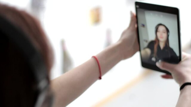 Young good looking woman with long hait in headphones uses multitouch screen tablet to take a selfie photograph