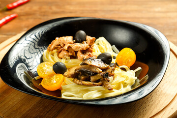 Black plate with spaghetti nests stuffed with assrty chicken fillet and mushrooms on a stand.