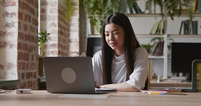 Young asian girl greeting with groupmates via video chat on laptop