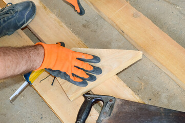 construction site - the worker holds in his hand a sawed-off part of the board, next to it is a saw and a tape measure