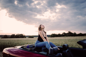 cute girl is sitting in a convertible in the summer on a trip.