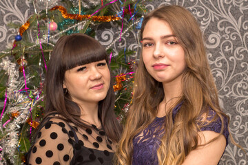 Two beautiful girls are standing against the background of the New Year tree.