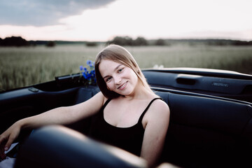 cute girl is sitting in a convertible in the summer on a trip.