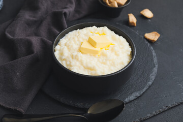 Bowl with boiled rice and butter on dark background