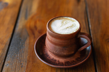 Coffee with milk or cappuccino in brown clay mug on wooden table. 