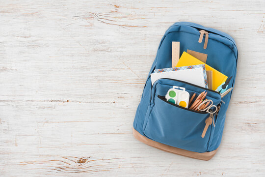 Backpack with different school supplies isolated on vintage wooden background