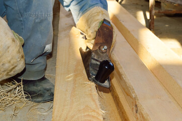 a man in white gloves planes a wooden board with a planer, aligns it