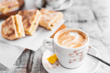 Traditional breakfast - a cup of coffee with milk and cheese and ham sandwich on the background