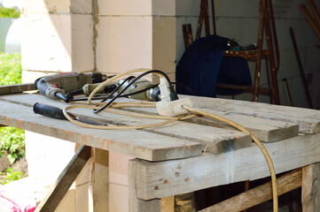 close-up - a white extension cord lies on a table made of old boards against the background of working tools and a construction site