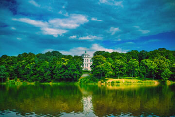 Fototapeta na wymiar Beautiful landscape of park with manor in summertime. Picturesque place of white Palace with pond and green trees.