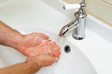 Close up photo of male hands washing with soap above the sink