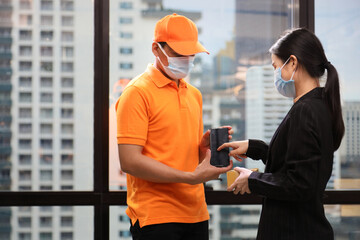 Business woman digitally signing for the received package from online order from delivery man in the urban company office with skyscraper view on the back