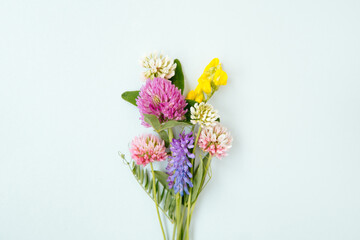 Small bouquet of miniature wildflowers on blue background in the centre, copyspace for summer and wedding design. Boutonniere from clover and mouse pease