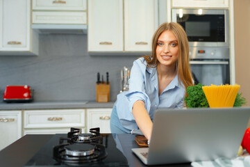 Young blonde woman with long hair using laptop in a kitchen