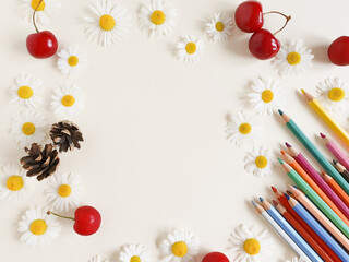 Colored pencils, paper, camomiles, cherry berries and fir cones on a ivory background. Top view, Frame. Empty space for a text. Lifestyle, mock-up.