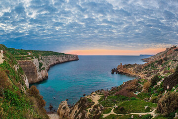 Fototapeta na wymiar Colourful clouds saturate the background at Fomm ir-Rih, Malta